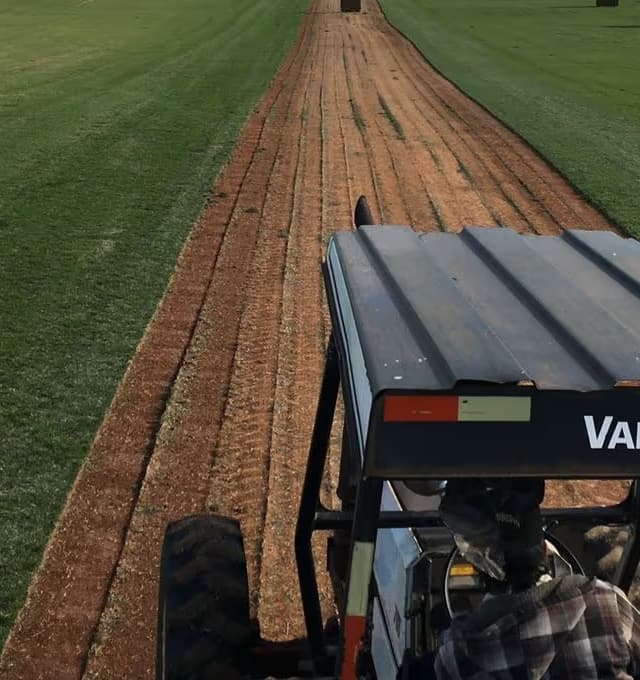 Trator colhendo uma faixa de grama, com a terra vermelha exposta no meio do campo